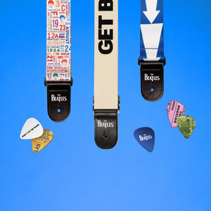 Three Beatles-themed guitar straps are arranged on a bright blue background with several guitar picks scattered around. 