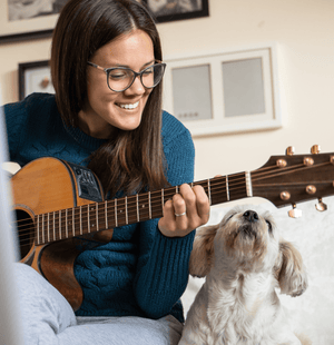 Woman playing guitar with a dog sitting next to her